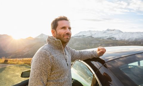 A man in gray half-zip pullover sweater placing his arm on his car in the outdoors.