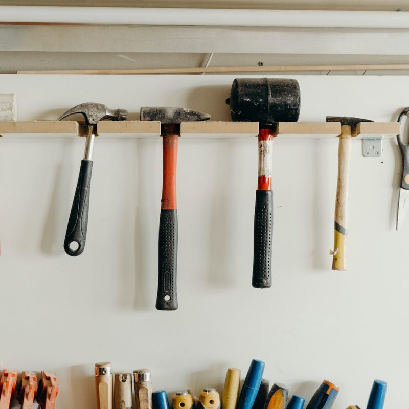 Tools hanging on white wall by a thin piece of wood.