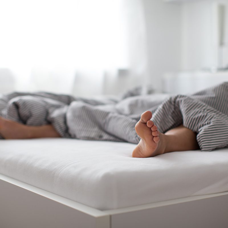 Person sleeping with their feet sticking out from the comforter