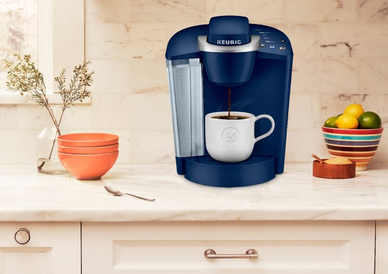A blue Keurig K-Classic Single Serve K-Cup Pod Coffee Maker placed on a kitchen countertop with plants nearby.