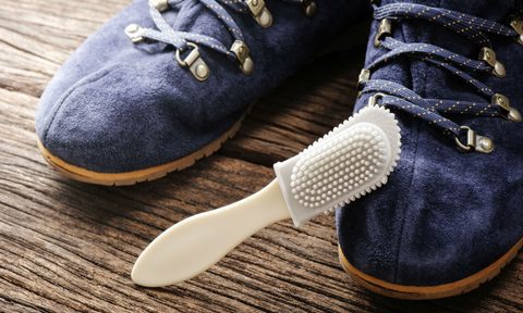 A plastic suede brush and a pair of blue suede shoes on wooden floor.