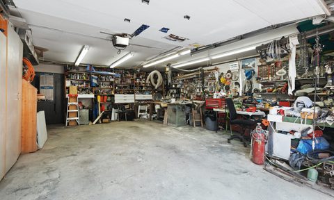 A cluttered garage with tools on shelves and a dirty floor.