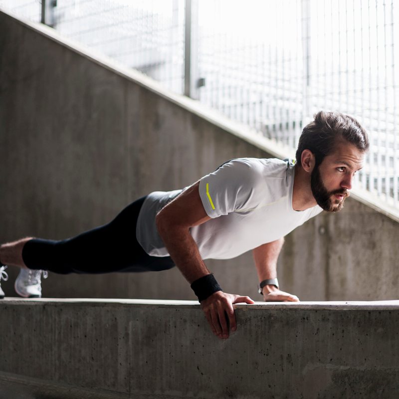 A man in white shirt, black jogging pants, and white shoes doing pushups on a concrete platform.