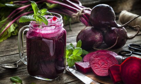 A glass of beet juice beside sliced and whole beets on a wooden table.