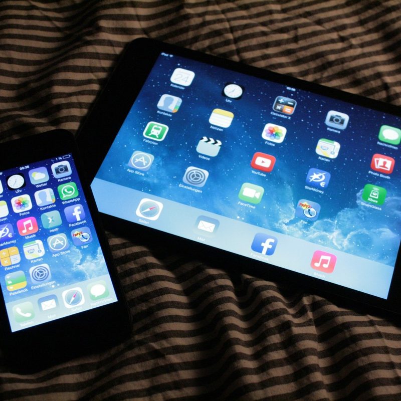 A smartphone and a tablet lie on a bed