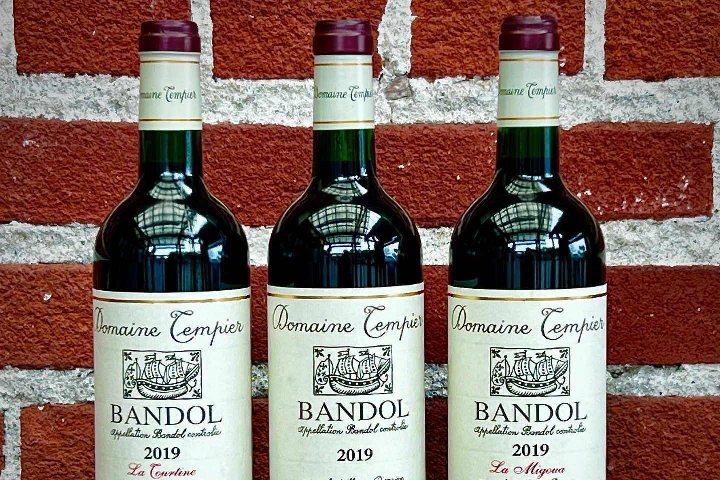 Three bottles of Domaine Tempier Bandol displayed against a brick wall.