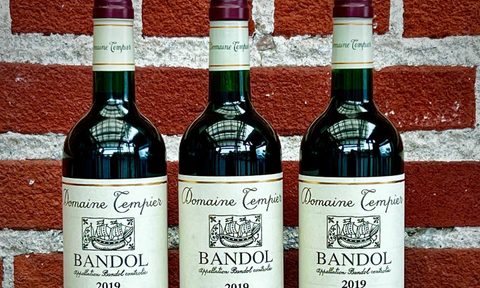 Three bottles of Domaine Tempier Bandol displayed against a brick wall.