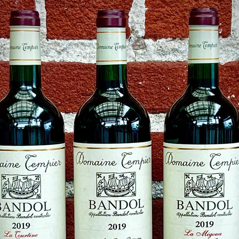 Three bottles of Domaine Tempier Bandol displayed against a brick wall.