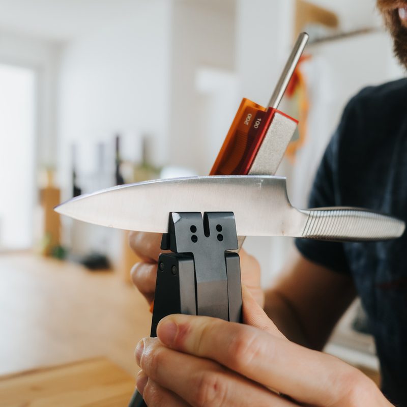 A man sharpening his knife with a knife sharpener at home.