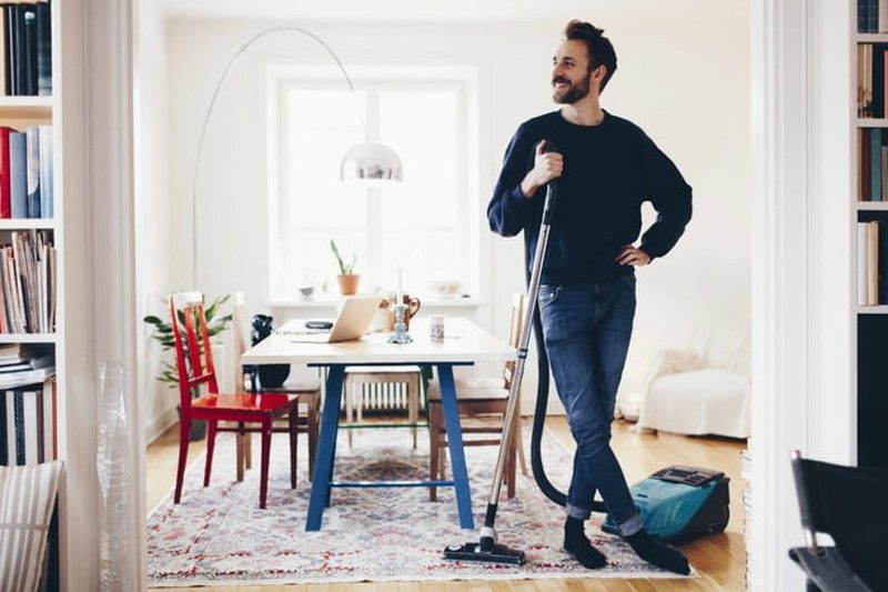 Man smiling in clean apartment holding a vacuum.
