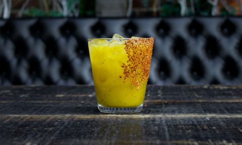 An ice-cold glass of Mango Basil Margarita on black table.