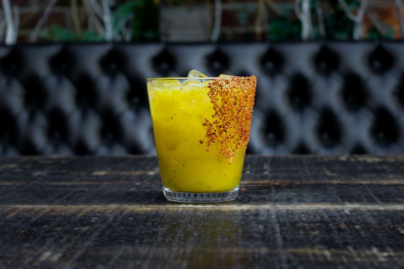 An ice-cold glass of Mango Basil Margarita on black table.