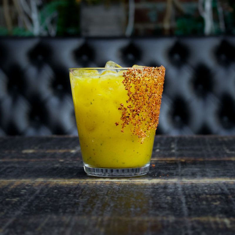 An ice-cold glass of Mango Basil Margarita on black table.