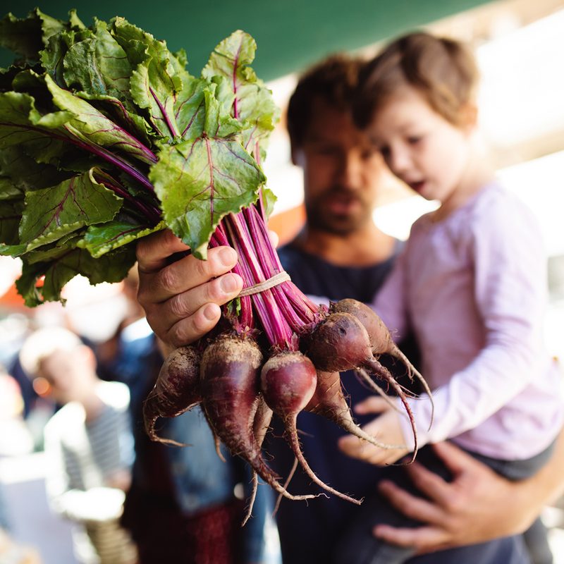A father holding a bunch of beets while carrying his son in the market.
