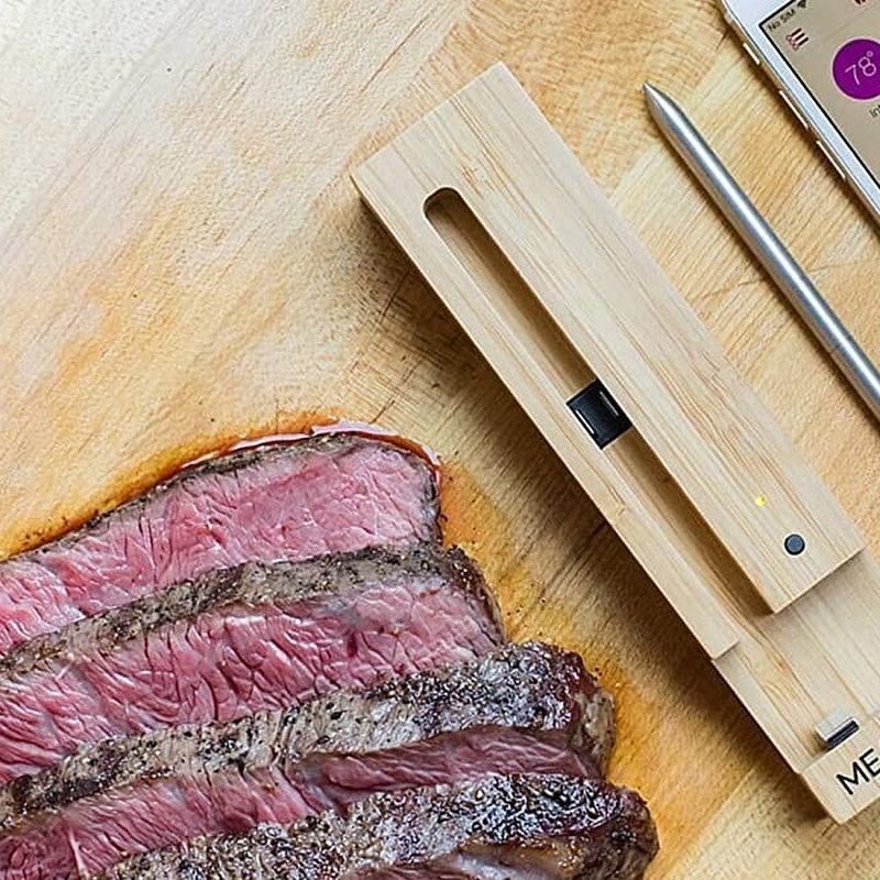 Meat slices beside a Meater Plus Smart Meat Thermometer on wooden table.