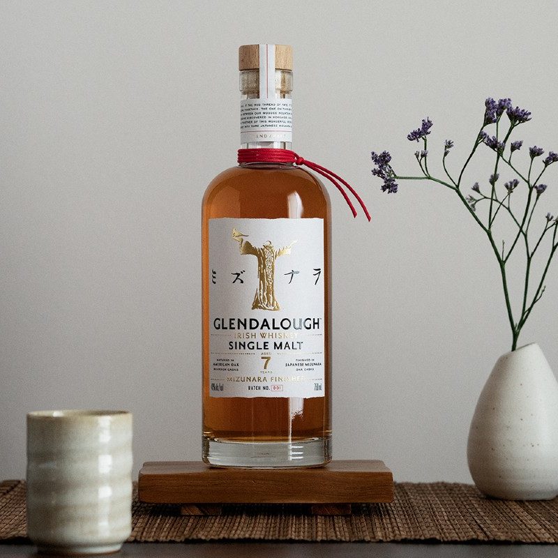 Glendalough Distillery's Mizunara Cask-Finished Whiskey bottle, along with a Japanese tea cup and flowers.