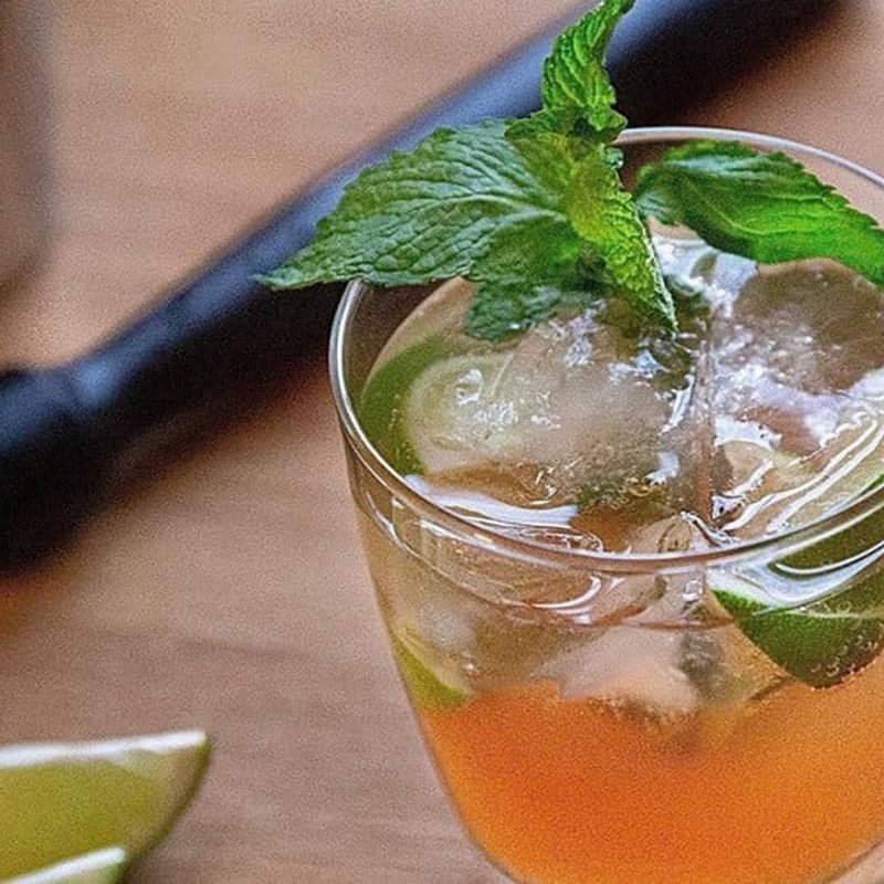 A close-up of a glass of Nectarine Mojito with mint leaves beside slices of lime.
