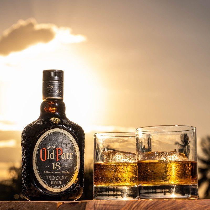 Old Parr Aged 18 Years Scotch, complete with rocks glasses, palm trees, and a sunset