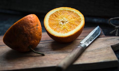 Orange sliced in half by knife on cutting board