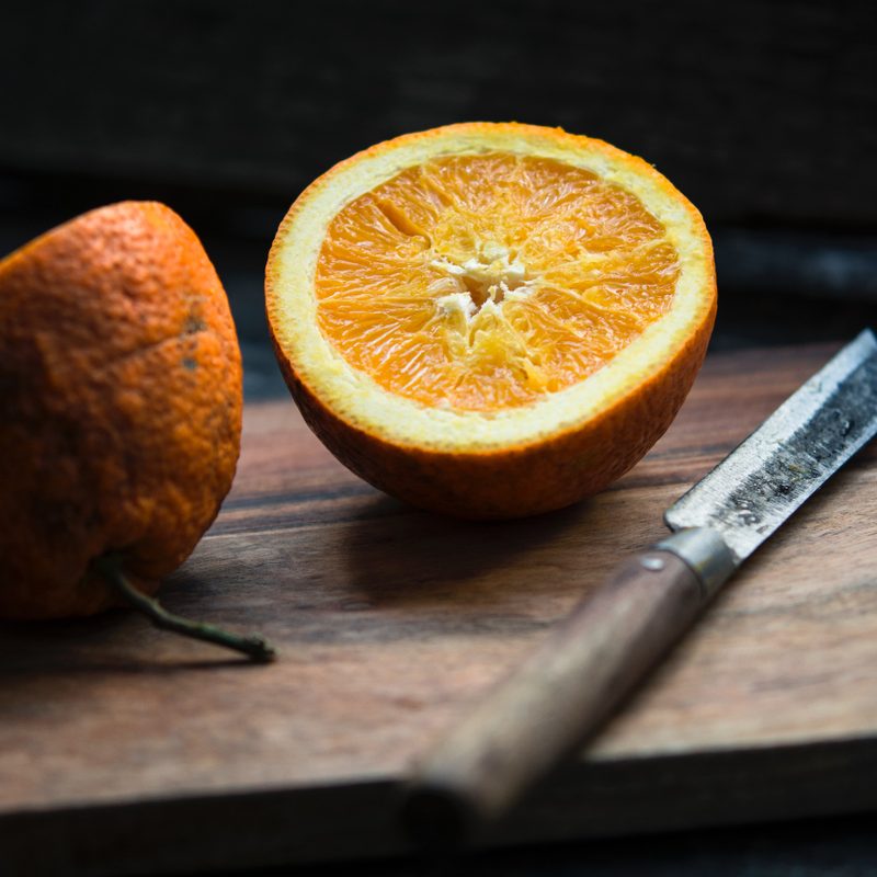 Orange sliced in half by knife on cutting board.