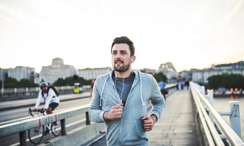 A man in jacket and earphones jogging on the street.