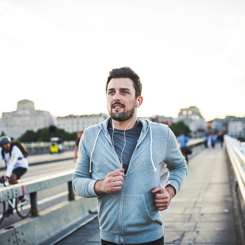 A man in jacket and earphones jogging on the street.