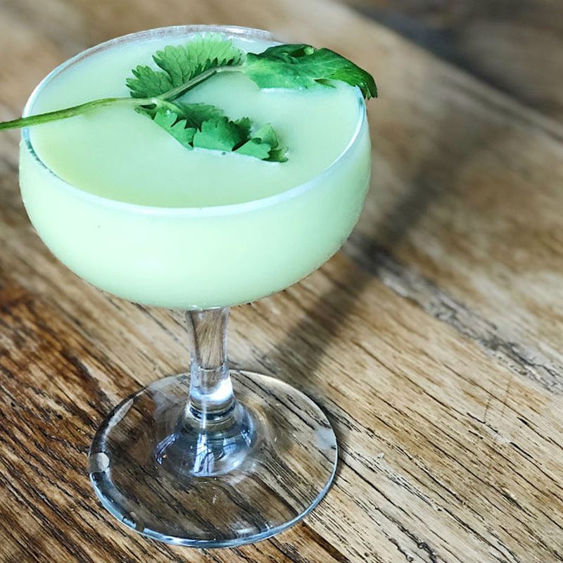 A glass of Pajaro Verde garnished with orange bitters on wooden table.