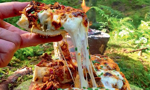 Polish Zapiekanka slice being lifted from the whole pastry in the woods.