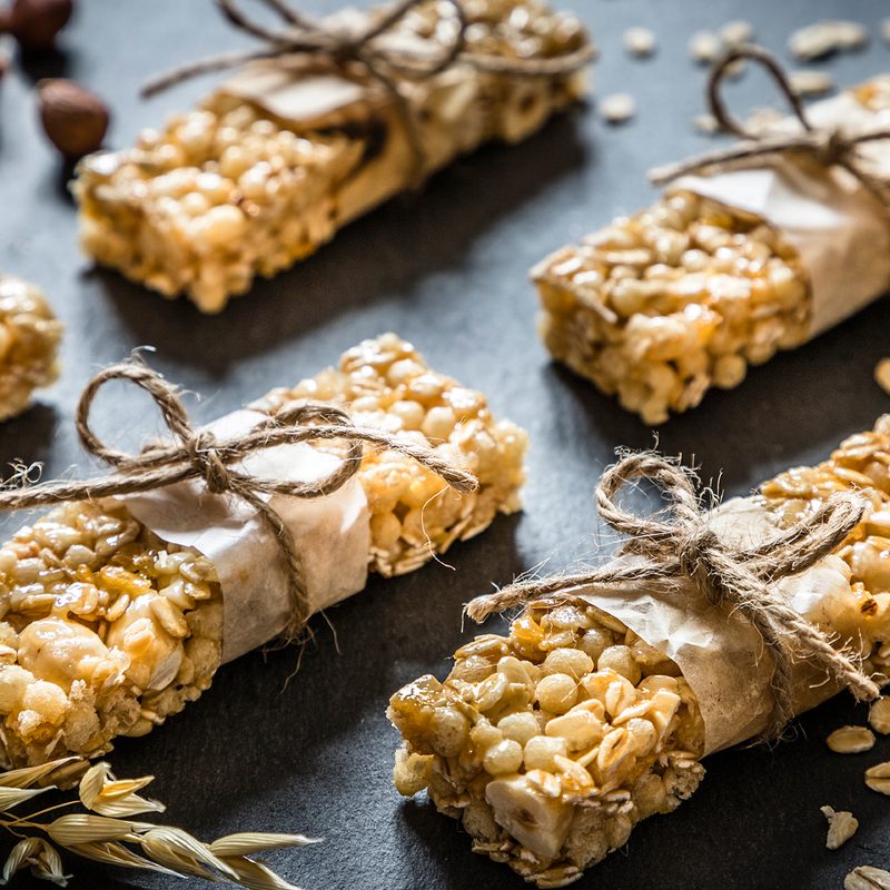 Five energy bars with nuts surrounding them on a black table.