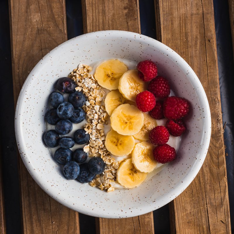 An overhead shot of a bowl of oatmeal with berries and banana slices on a wooden table.
