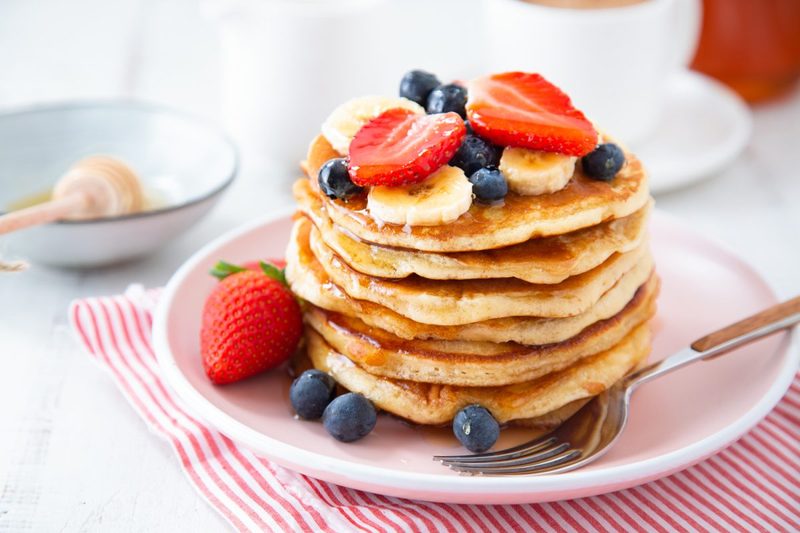 A pancake with strawberries, blueberries, and banana slices on a striped cloth on a table.