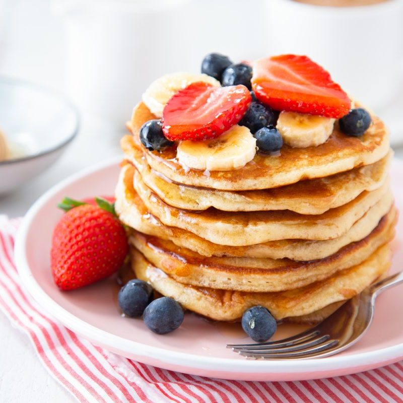 A pancake with strawberries, blueberries, and banana slices on a striped cloth on a table.