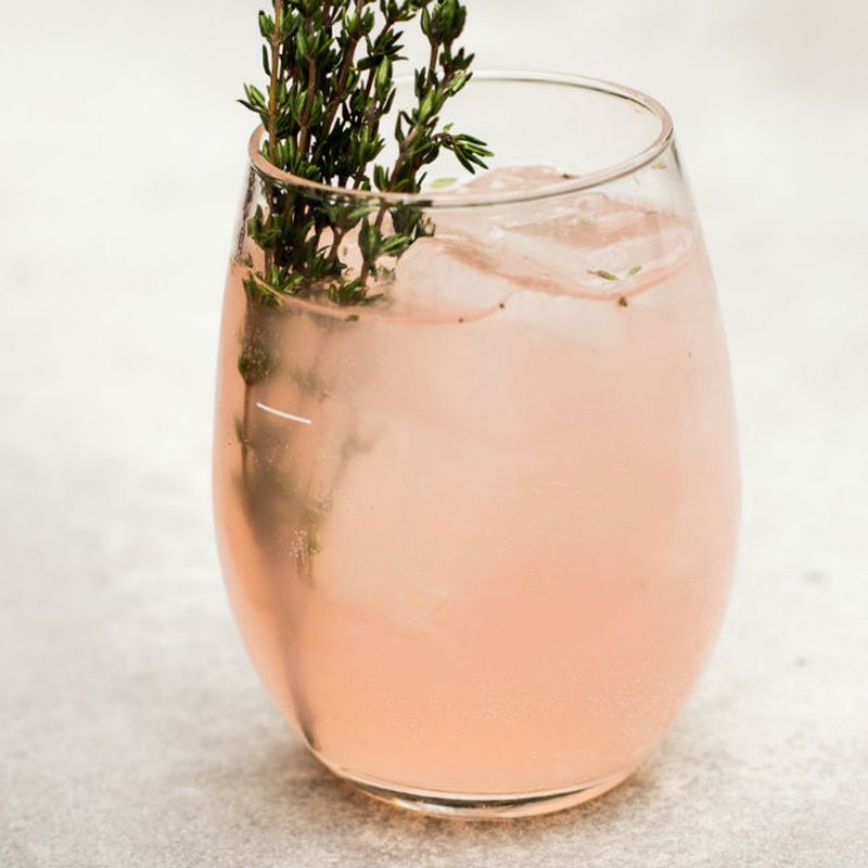 A glass of rooftop rosé spritz garnished with thyme on a table