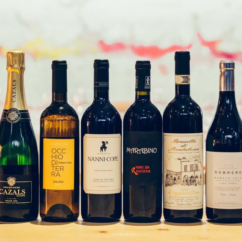 Six bottles of wine on a table in a dining area.