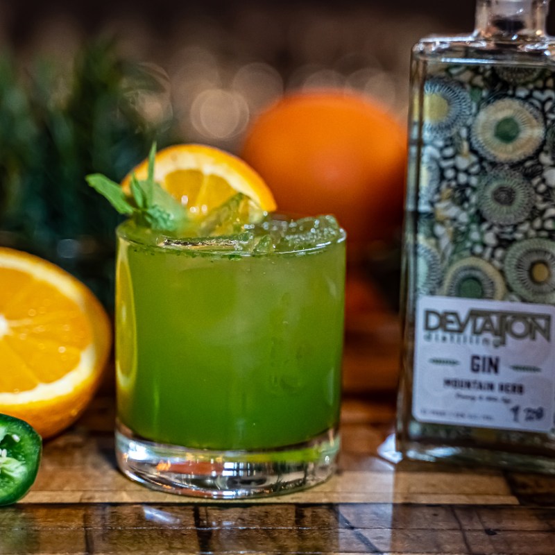 Spicy Leprechaun cocktail with orange slice, bottle of gin in background.