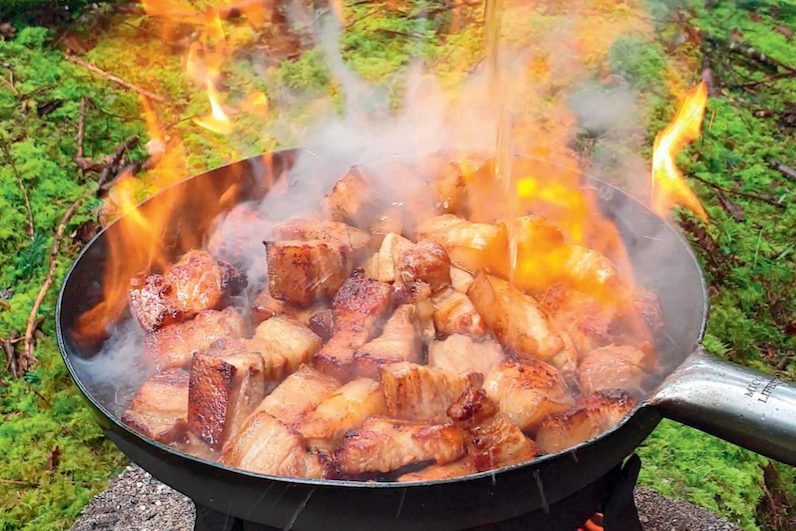 Sticky pork belly being cooked in a cast iron pan in the woods.