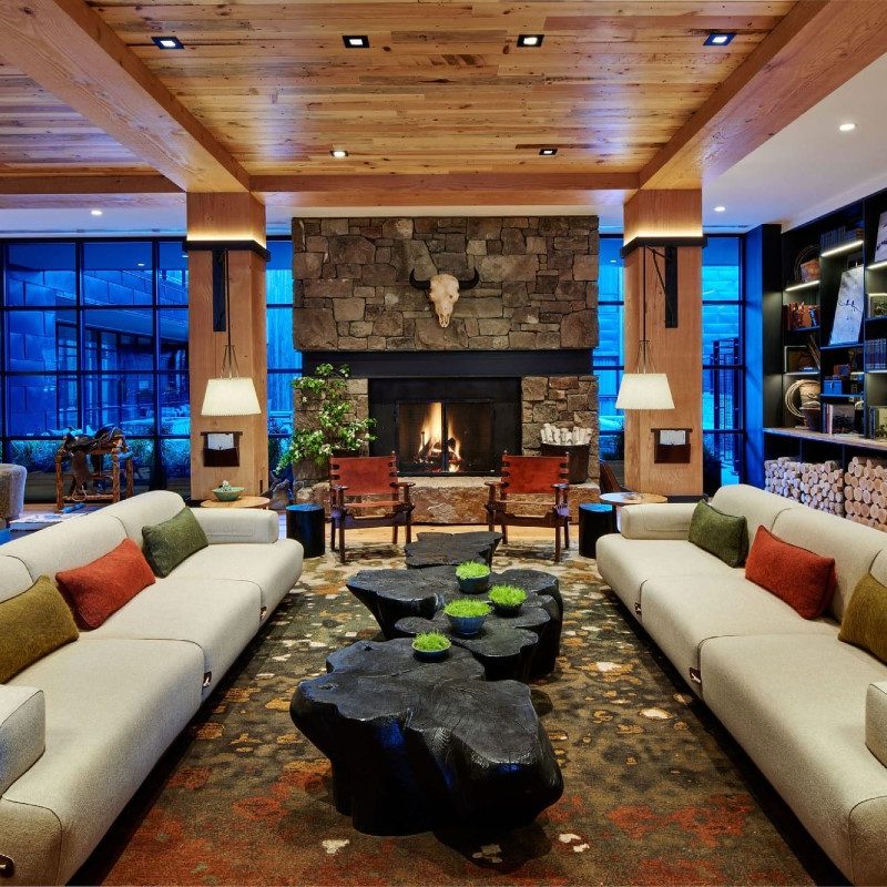 The Cloudveil lobby with sprawling couches, reclaimed wood ceilings, and granite shelving all surrounding a massive fieldstone fireplace, topped with a typical Western cow skull
