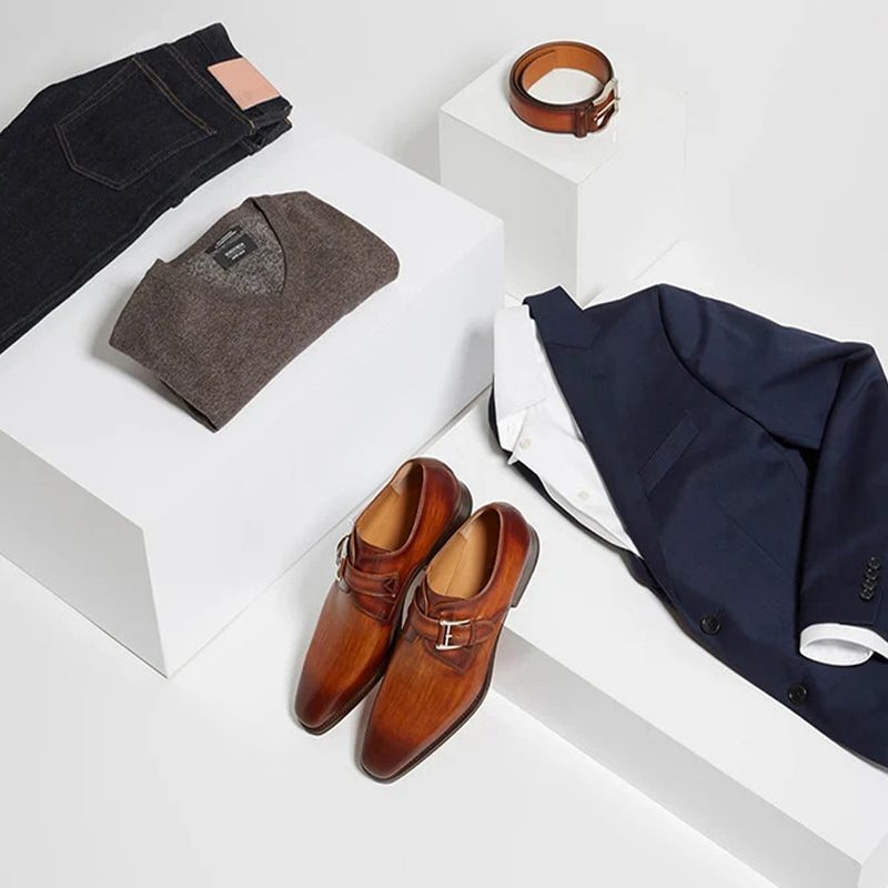 A folded jeans, suit, and t-shirt with belt and shoes on white platforms.