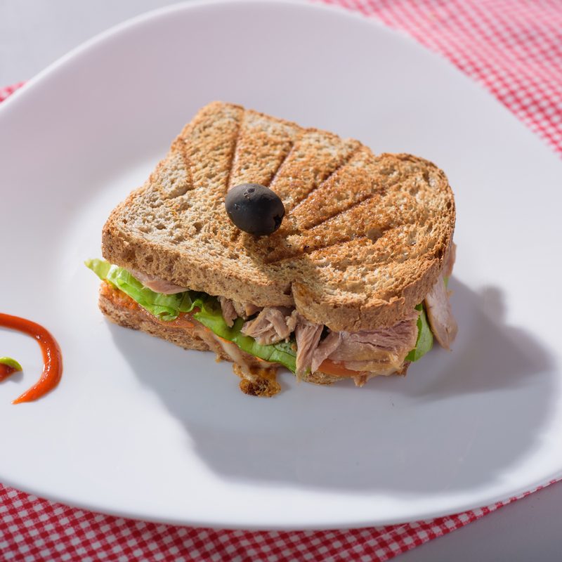 A toasted sandwich with tuna and veggies and sauce on a plate on red and white cloth.