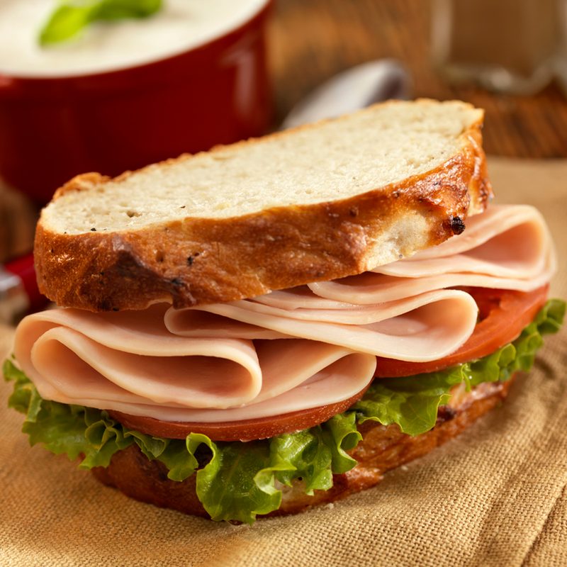 A turkey sandwich with vegetables on brown cloth and a bowl of mushroom soup in the background.
