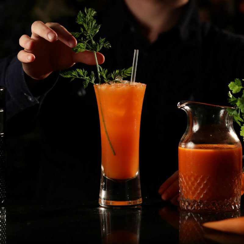 A bartender garnishing a What's Up Brock Cocktail coriander leaves beside a pitcher of What's Up Brock cocktail and a bottle of Brockman's gin.