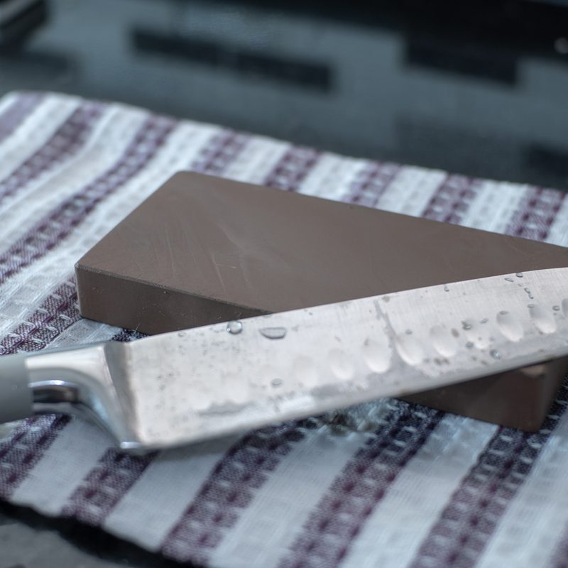 A steel knife and a whetstone on striped cloth.