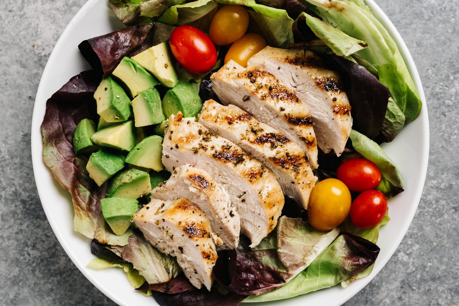 An overhead shot of a bowl of grilled chicken salad on a table