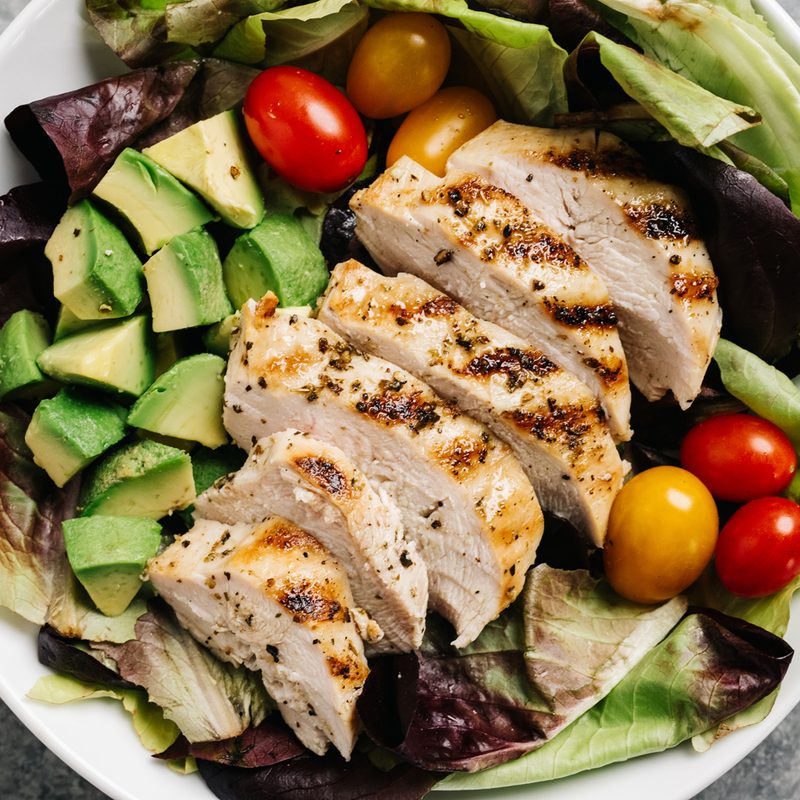 An overhead shot of a bowl of grilled chicken salad on a table.