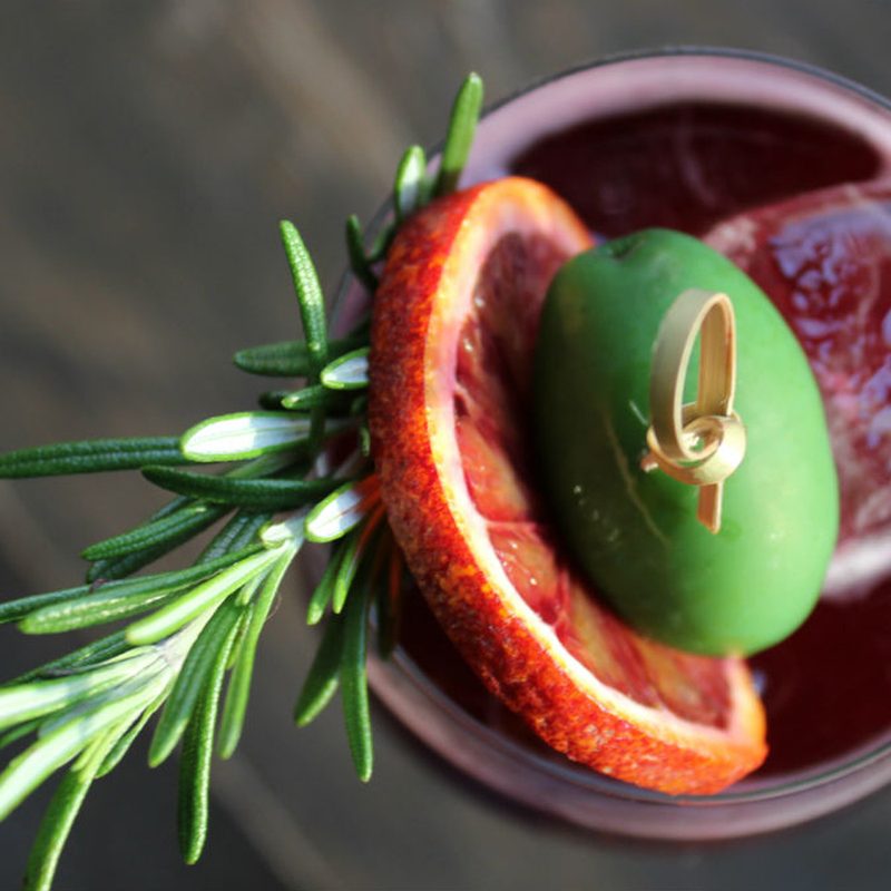 An overhead shot of Winter Spritz garnished with blood orange wheel, green olive, and rosemary sprig.