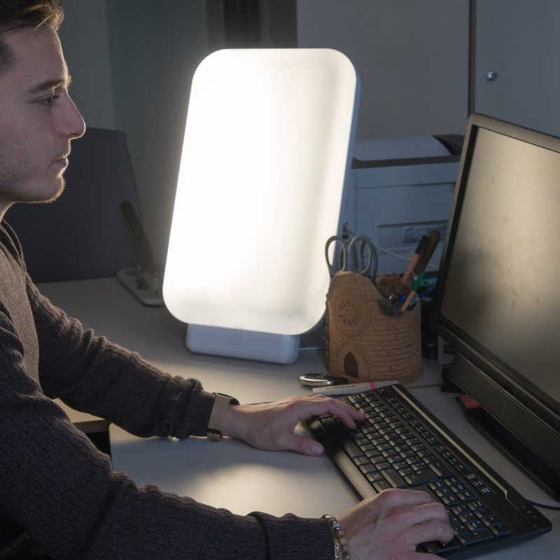 A young man works in his office with a light therapy lamp