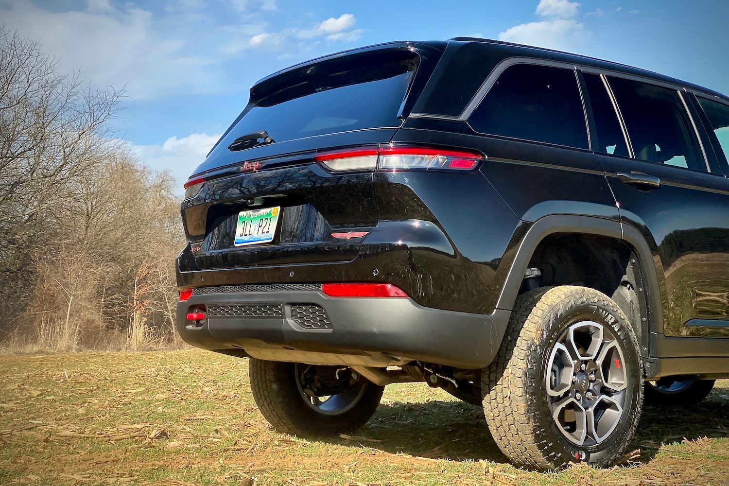 Close up of rear end of 2022 Jeep Grand Cherokee Trailhawk on a grassy field with trees in the background.