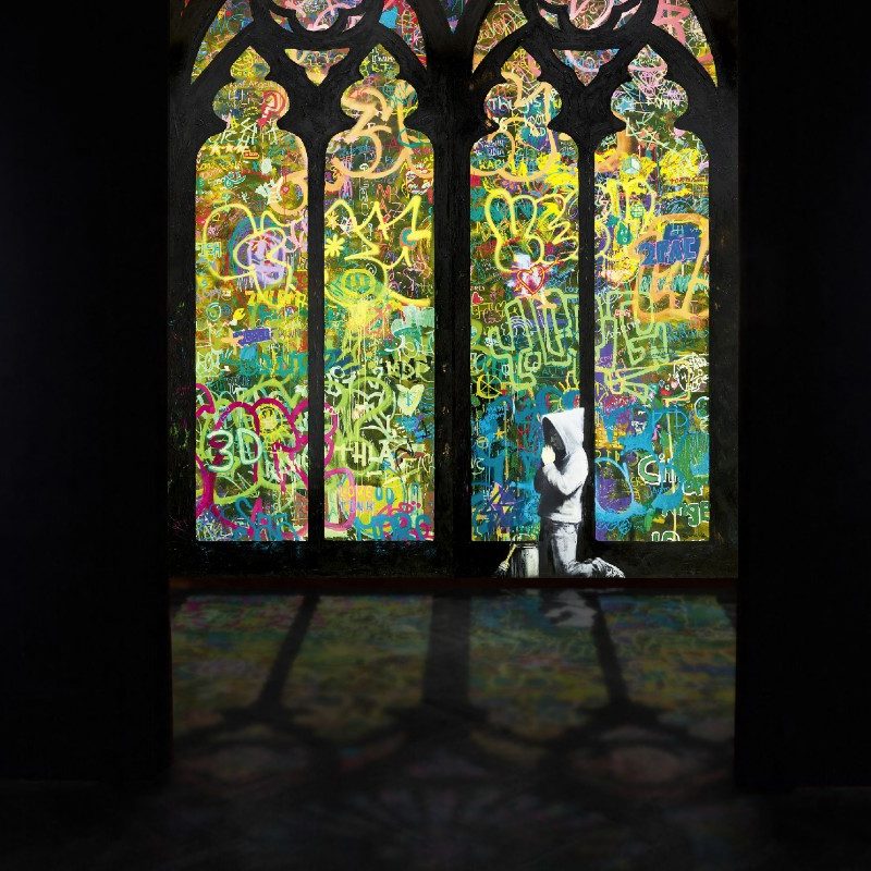 A stenciled black and white child prays before stained glass windows in the new 'Banksyland' exhibit showing in Portland and across the United States.
