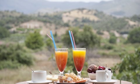 An outdoor breakfast spread that includes a pair of orange juices mixed with coffee.