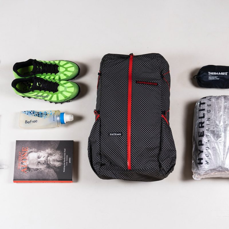 A lightweight backpacking setup including trainers, on a plain background.